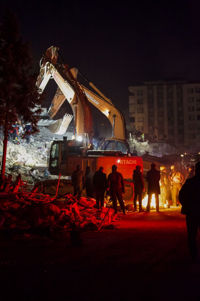 Excavators work through the night at a construction site surrounded by debris and workers.